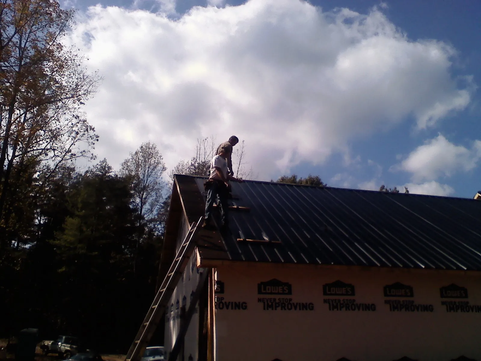 Roofer fastening dark metal panels high against a cloudy sky, from a Roof Inspection job in Haddam